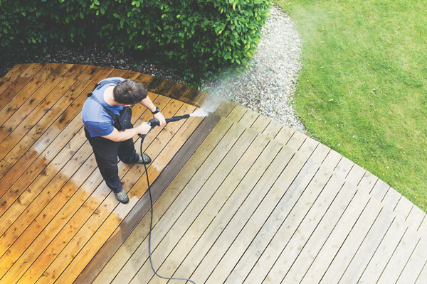 Homme qui nettoie sa terrasse en bois à l'aide d'un pulvérisateur à haute pression