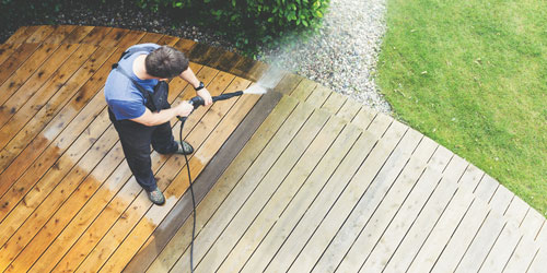Homme qui nettoie sa terrasse en bois à l'aide d'un pulvérisateur à haute pression